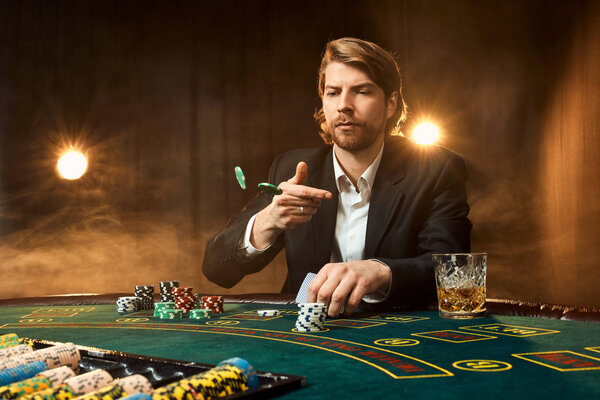 A man in a business suit sitting at the game table. Male player. Passion, cards, chips, alcohol, dice, gambling, casino - it is as male entertainment.