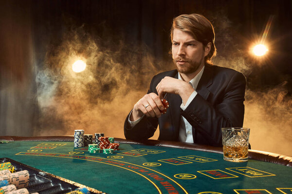A man in a business suit sitting at the game table. Male player. Passion, cards, chips, alcohol, dice, gambling, casino - it is as male entertainment.