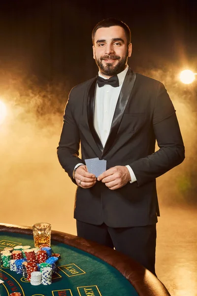 Un joven con un traje de negocios parado cerca de la mesa de póquer. El hombre apuesta . —  Fotos de Stock