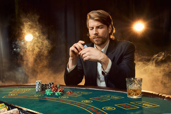 A man in a business suit sitting at the game table. Male player. Passion, cards, chips, alcohol, dice, gambling, casino - it is as male entertainment.