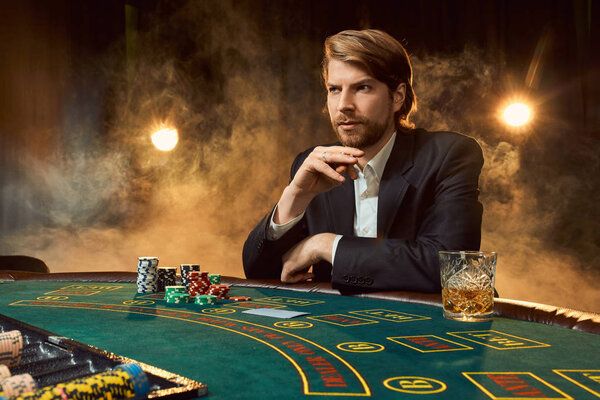 A man in a business suit sitting at the game table. Male player. Passion, cards, chips, alcohol, dice, gambling, casino - it is as male entertainment.