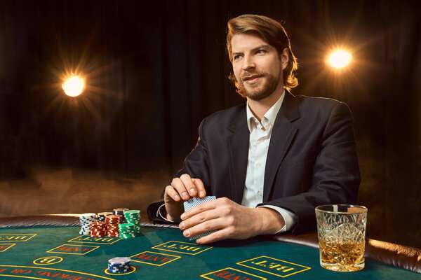 A man in a business suit sitting at the game table. Male player. Passion, cards, chips, alcohol, dice, gambling, casino - it is as male entertainment.