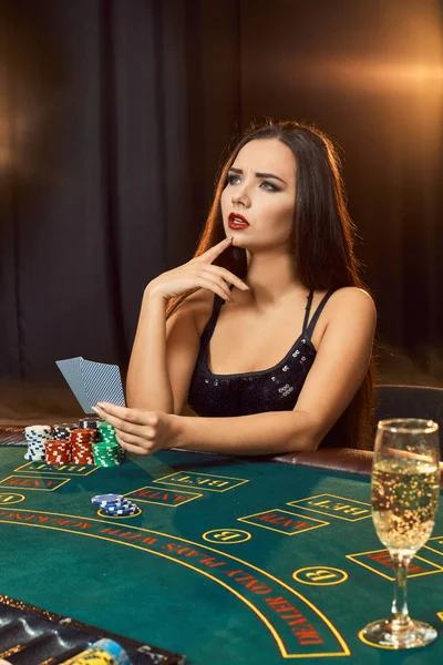 Wanita muda cantik duduk di meja poker dengan segelas sampanye — Stok Foto