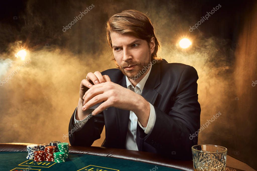 A man in a business suit sitting at the game table. Male player. Passion, cards, chips, alcohol, dice, gambling, casino - it is as male entertainment. Dangerous fun card game for money. Let the smoke.