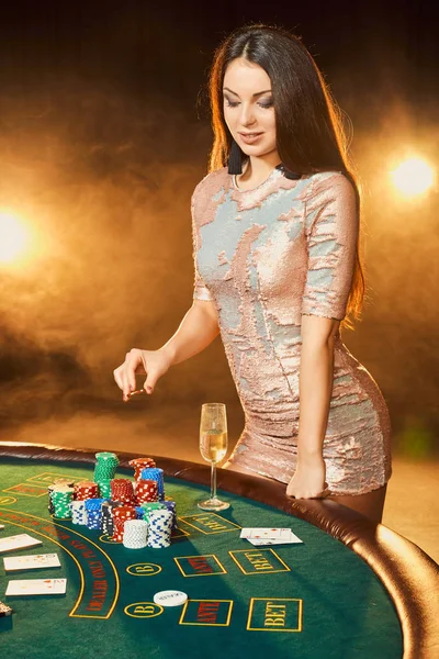 Vacker ung kvinna i aftonklänning stående nära pokerbord med glas champagne — Stockfoto