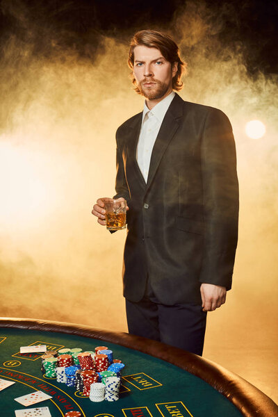 A young man in a business suit standing near poker table. Man gambles.