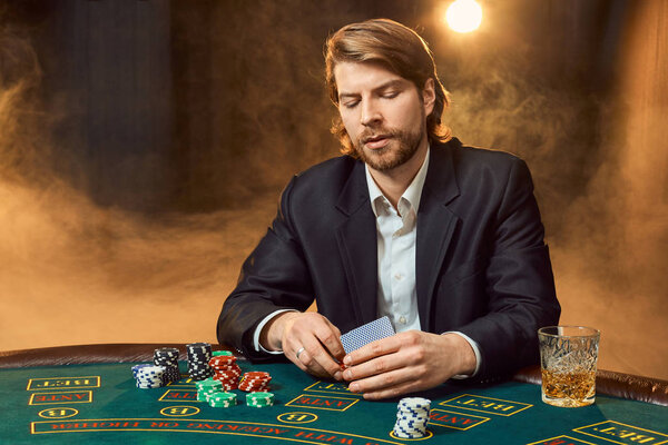 A man in a business suit sitting at the game table. Male player. Passion, cards, chips, alcohol, dice, gambling, casino - it is as male entertainment.