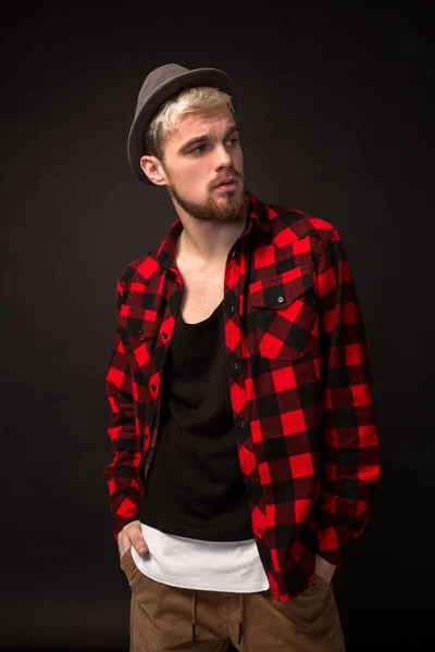 Guapo joven de moda en el estudio sobre fondo negro. Lleva barba y camisa a cuadros. — Foto de Stock