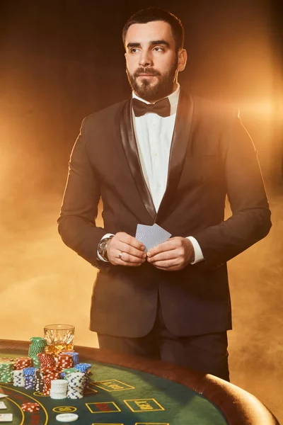 Un joven con un traje de negocios parado cerca de la mesa de póquer. El hombre apuesta . —  Fotos de Stock