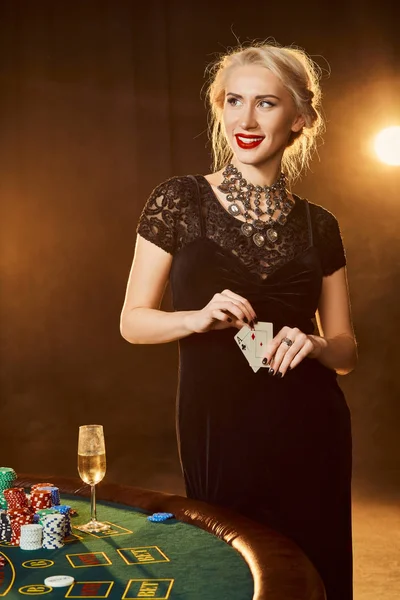 Siyah elbiseli bir kadın onun elinde kartları ile poker masasında duruyor — Stok fotoğraf
