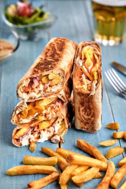 Shawarma tavuk rulo bir pide taze sebze, krema sos ve patates kızartması ile ahşap arka plan üzerinde. Seçici odak