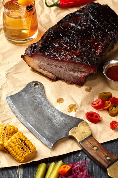 Frische Brisket BBQ Rindfleisch in Scheiben geschnitten zum Servieren vor einem Kraftpapier Hintergrund mit Sauce, Paprika und Mais. — Stockfoto