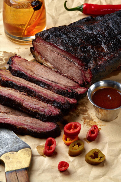 Fresh Brisket BBQ beef sliced for serving against a kraft paper background with sauce, hot peppers and corn.