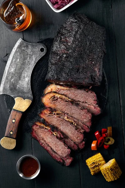 Fresh Brisket BBQ beef sliced for serving against a dark background with sauce, hot peppers and corn. — Stock Photo, Image