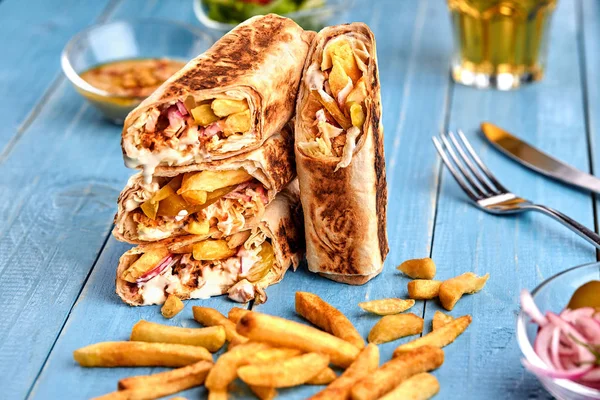 Shawarma tavuk rulo bir pide taze sebze, krema sos ve patates kızartması ile ahşap arka plan üzerinde. Seçici odak