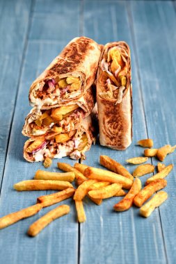 Shawarma tavuk rulo bir pide taze sebze, krema sos ve patates kızartması ile ahşap arka plan üzerinde. Seçici odak