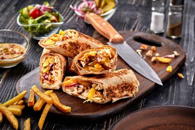 Shawarma tavuk rulo bir pide taze sebze, krema sos ve patates kızartması ile ahşap arka plan üzerinde. Seçici odak