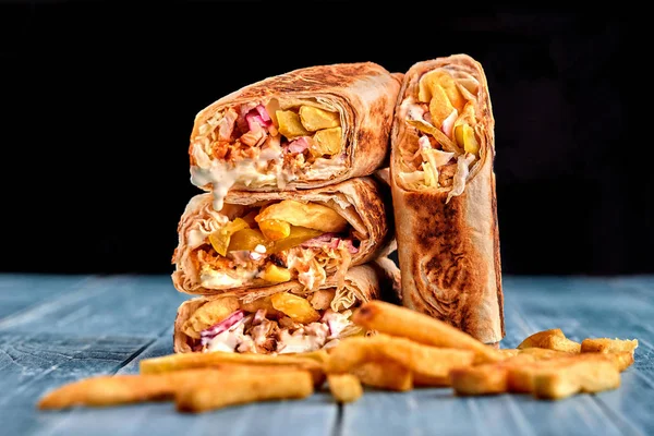 Shawarma tavuk rulo bir pide taze sebze, krema sos ve patates kızartması ile ahşap arka plan üzerinde. Seçici odak
