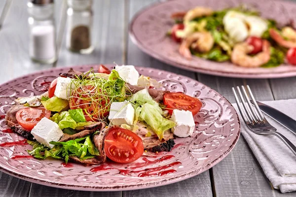 Gezonde gemengde Griekse salade geserveerd op een roze plaat met zilveren vork met scherpe lommerrijke Groenen, microgreen, feta, ui, tomaat en gesneden rundvlees — Stockfoto