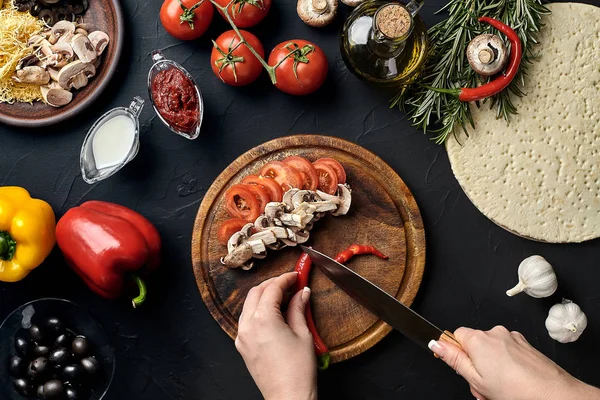Chile cortado a mano femenino, champiñones y tomates sobre tabla de madera en la mesa de la cocina, alrededor de los ingredientes de la mentira para la pizza: verduras, queso y especias . — Foto de Stock