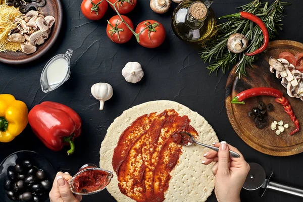Manos de panadero agregando ingredientes a la pizza durante la preparación de la pizza en la cocina — Foto de Stock
