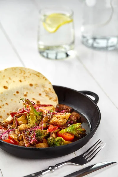 Rostade grönsaker - potatis, gröna bönor, morot och paprika i svart järn plattan på vitt trä bord. — Stockfoto