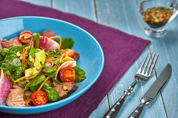 Baharatlı sığır eti dilim et salata domates, maydanoz, turp ve salata ile ahşap bir masa üzerinde mavi bir tabak içinde ıspanak yaprakları.