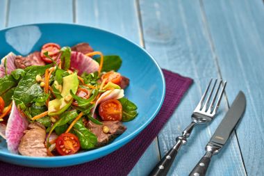 Baharatlı sığır eti dilim et salata domates, maydanoz, turp ve salata ile ahşap bir masa üzerinde mavi bir tabak içinde ıspanak yaprakları.