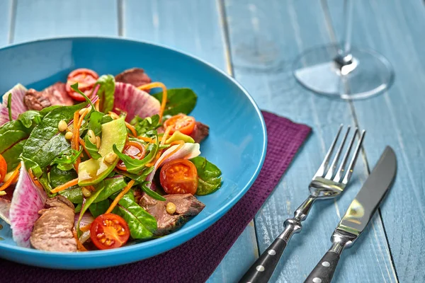 Baharatlı sığır eti dilim et salata domates, maydanoz, turp ve salata ile ahşap bir masa üzerinde mavi bir tabak içinde ıspanak yaprakları.