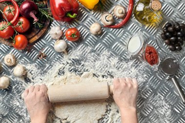Eller üzerinde metal arka plan dışarı hamur rulo, yakın çekim. Şef hamur yapar. Sebze ve mutfak eşyaları içeren tablo. İtalyan mutfağı kavramı. Pizza