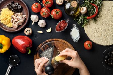 Peynir ovuşturdu eller pizza, pizza siyah tablo, üstten görünüm üzerinde yemek pişirmek için malzemeler rendelenmiş.