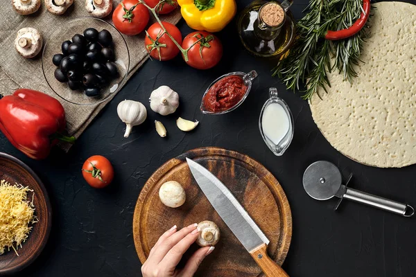 Las setas femeninas cortadas a mano en el tablero de madera en la mesa de la cocina, alrededor de los ingredientes de mentira para la pizza: verduras, queso y especias . — Foto de Stock