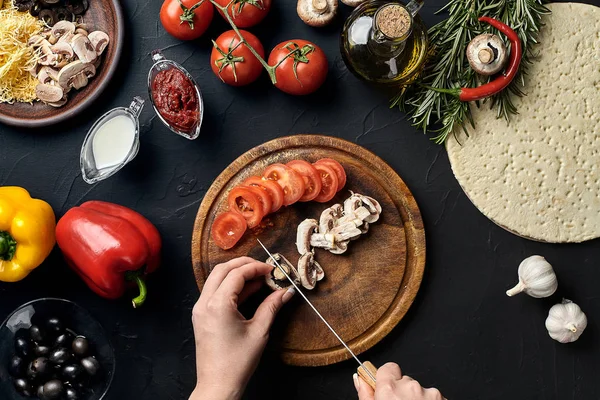 Hembra hongos cortados a mano y tomates en tablero de madera en la mesa de la cocina, alrededor de la mentira ingredientes para la pizza: verduras, queso y especias . — Foto de Stock