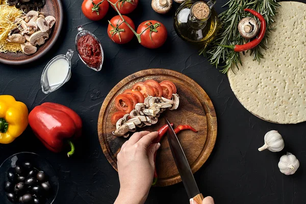 Chile cortado a mano femenino, champiñones y tomates sobre tabla de madera en la mesa de la cocina, alrededor de los ingredientes de la mentira para la pizza: verduras, queso y especias . — Foto de Stock