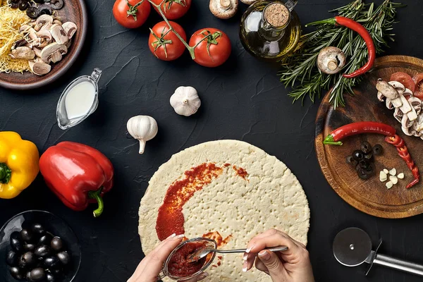 Manos de panadero agregando ingredientes a la pizza durante la preparación de la pizza en la cocina — Foto de Stock