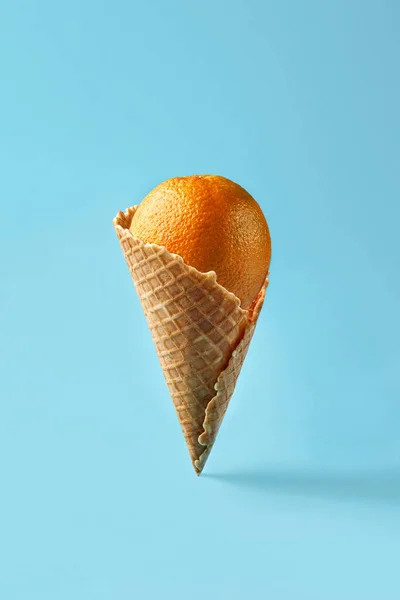 Naranja como el helado se encuentra en el cono de gofre sobre un fondo azul claro. Patrón — Foto de Stock