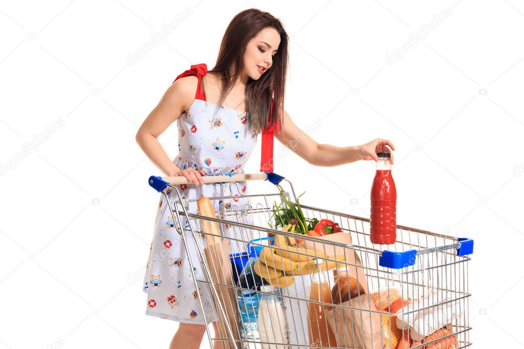 Smiling young woman doing grocery shopping at the supermarket, she is putting a tomato juice bottle in the cart