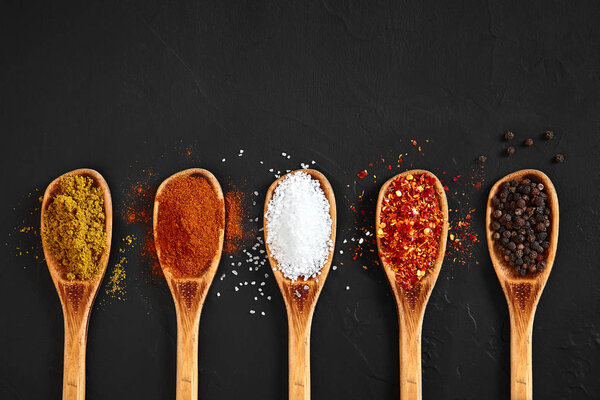 Различные специи в деревянных ложках на черном столе
