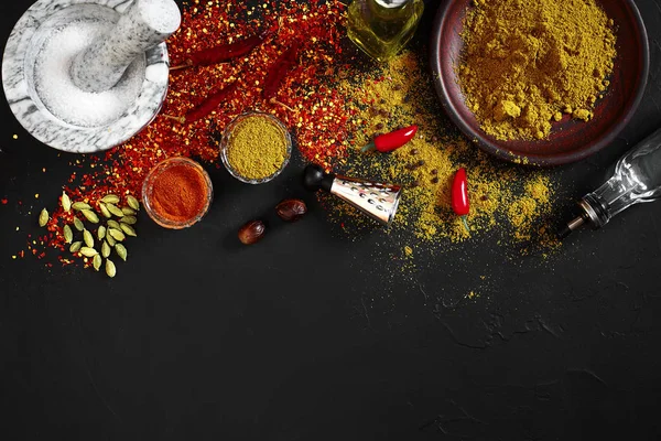 Cocinar con especias molidas frescas con mortero y tazones pequeños de especias en una mesa negra con derrame de polvo en su superficie, vista aérea con espacio para copiar — Foto de Stock