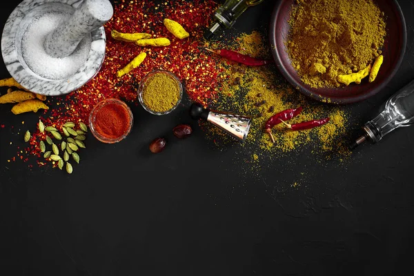 Cocinar con especias molidas frescas con mortero y tazones pequeños de especias en una mesa negra con derrame de polvo en su superficie, vista aérea con espacio para copiar — Foto de Stock