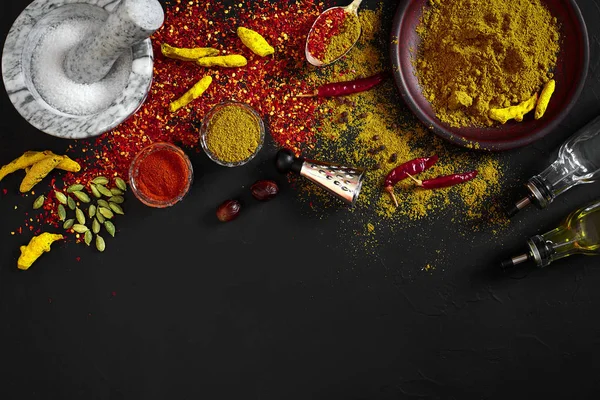 Matlagning med färskmalen kryddor med murbruk och små skålar av spice på ett svart bord med pulver spill på dess yta, overhead Visa med copyspace — Stockfoto