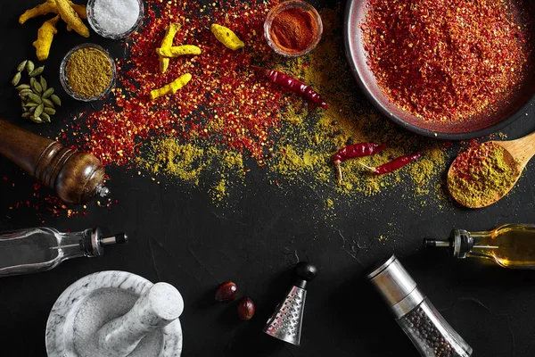 Cocinar con especias molidas frescas con mortero y tazones pequeños de especias en una mesa negra con derrame de polvo en su superficie, vista aérea con espacio para copiar — Foto de Stock