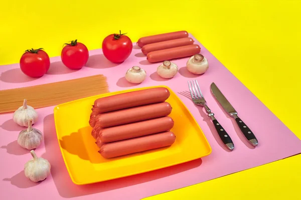 Un sacco di salsicce crude sul piatto. Su fondo rosa e giallo con pasta e verdure, vista dall'alto . — Foto Stock