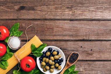 İtalyan makarna, spagetti, fesleğen, domates, zeytin ve zeytinyağı ahşap arka plan üzerinde hazırlanması için ham maddeler. Üstten Görünüm. Kopya alanı.