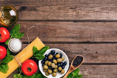 İtalyan makarna, spagetti, fesleğen, domates, zeytin ve zeytinyağı ahşap arka plan üzerinde hazırlanması için ham maddeler. Üstten Görünüm. Kopya alanı.