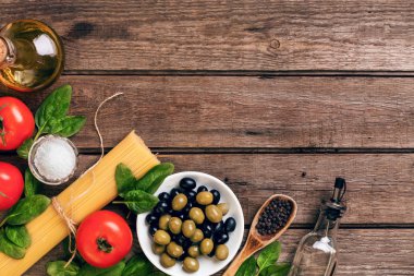 İtalyan makarna, spagetti, fesleğen, domates, zeytin ve zeytinyağı ahşap arka plan üzerinde hazırlanması için ham maddeler. Üstten Görünüm. Kopya alanı.