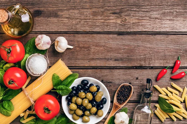 Raw ingredients for the preparation of Italian pasta, spaghetti, basil, tomatoes, olives and olive oil on wooden background. Top view. Copy space. — Stock Photo, Image