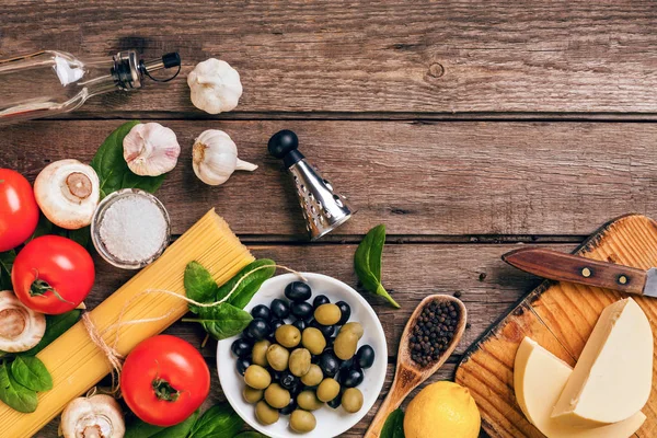 Grondstoffen voor de bereiding van Italiaanse pasta, spaghetti, basilicum, tomaten, olijven en olijfolie op houten achtergrond. Bovenaanzicht. Kopiëren van ruimte. — Stockfoto