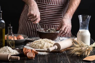 Erkek Şef ekmek ahşap masa üzerinde yumurta kırbaçlanan. Pişirme Unlu Mamüller veya hamur için malzemeler