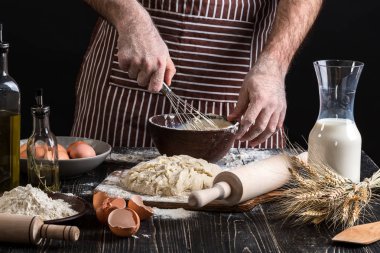 Erkek Şef ekmek ahşap masa üzerinde yumurta kırbaçlanan. Pişirme Unlu Mamüller veya hamur için malzemeler